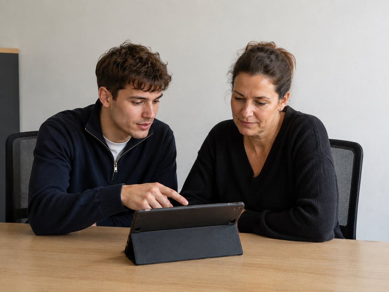 Zwei Personen sitzen an einem Tisch und schauen gemeinsam auf ein Tablet